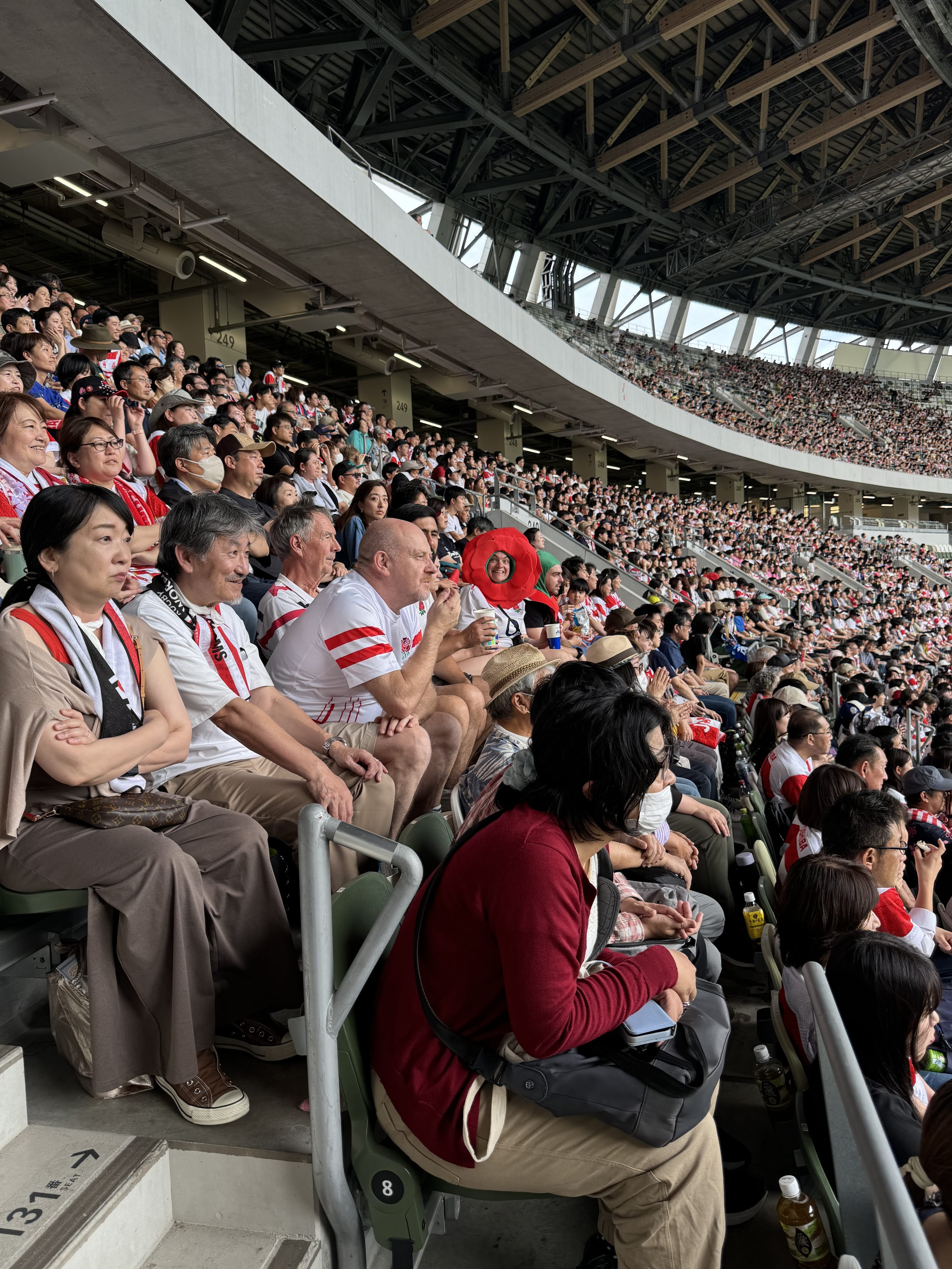 Picture of the crowd at a rugby match with one of the NRT team wearing a Rose on her head